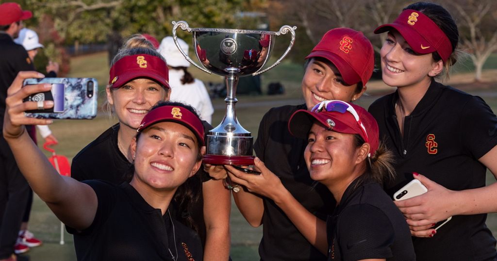 Malia Nam with a team of golfers holding a silver trophy and taking a group selfie